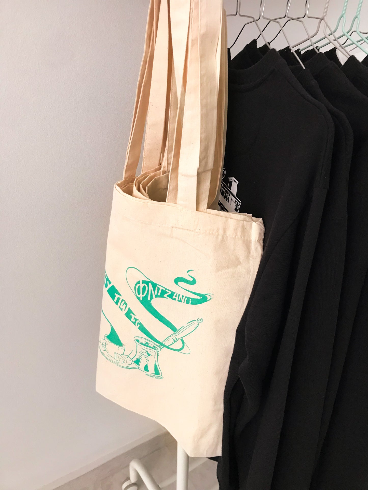 Tote bags hang on a coat rack with some sweat shirts