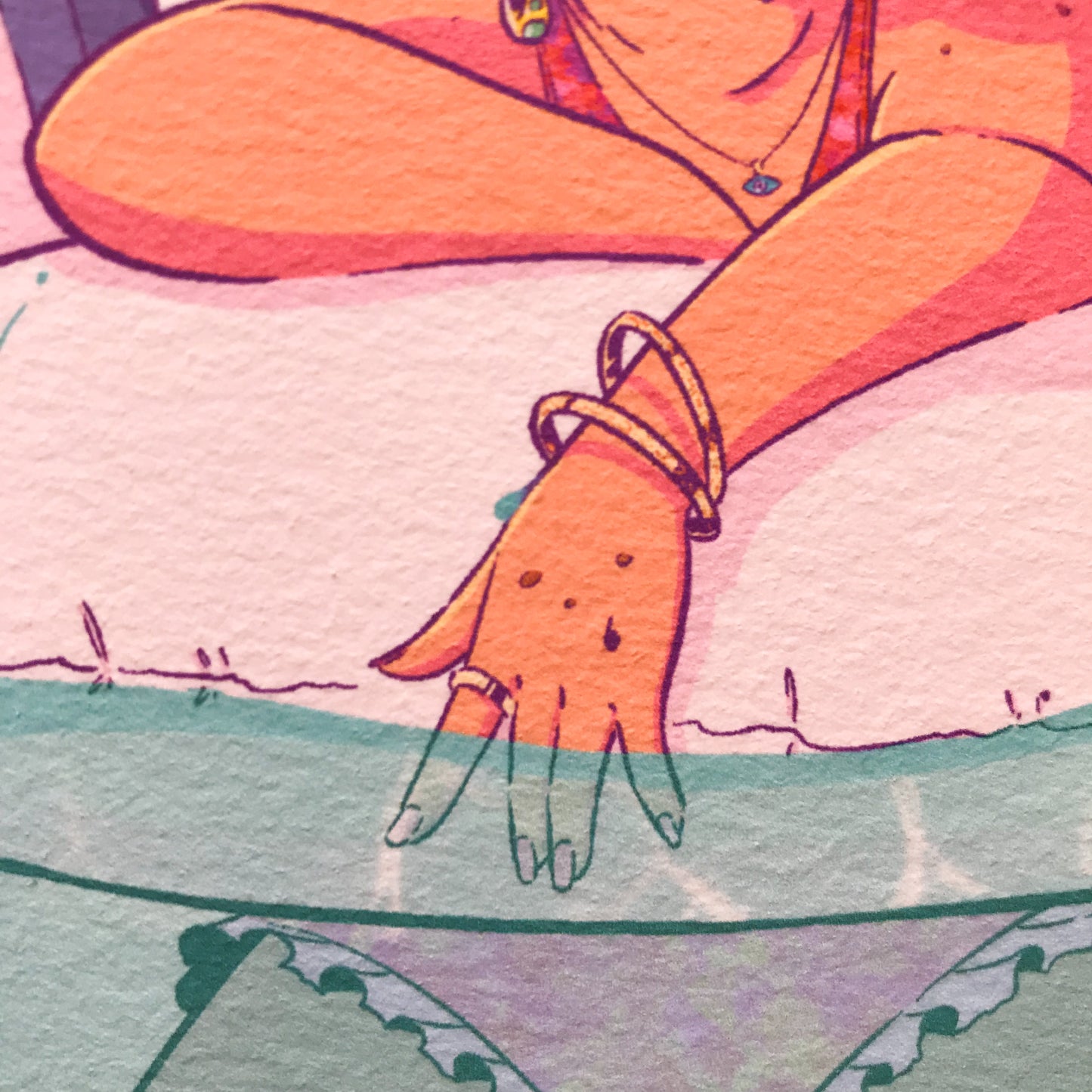 Close up on the hand of the lady. She’s wearing gold bracelets, and rings. And a necklace with an eye too. Her nails are painted in pink.