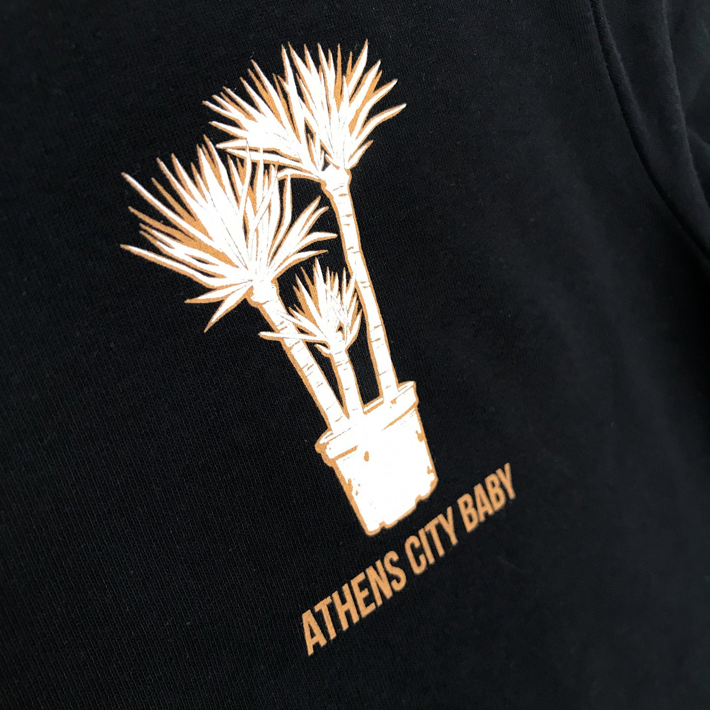 close up of the front design which is a yucca plant (three plant) in plastic pot. Under it it is written "Athens City Baby"