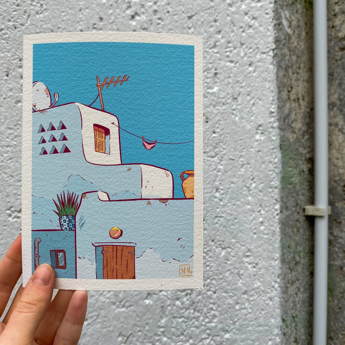 The print is hold by a hand in front of a wall, at the right of the picture we can see an air conditioning pipe.