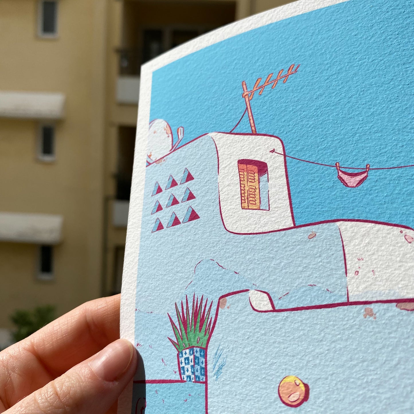 The print is hold by a hand in front of a building.
