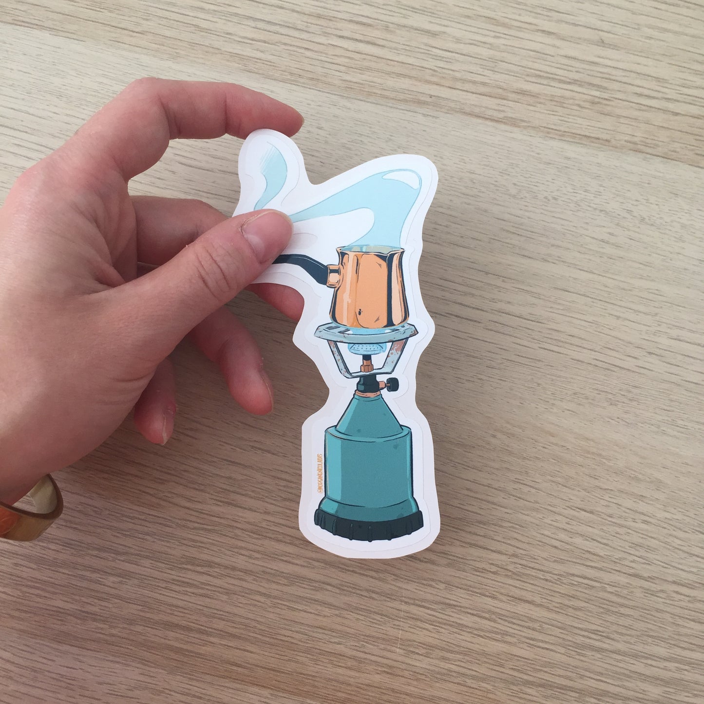 The sticker is held by a hand above a wooden table.