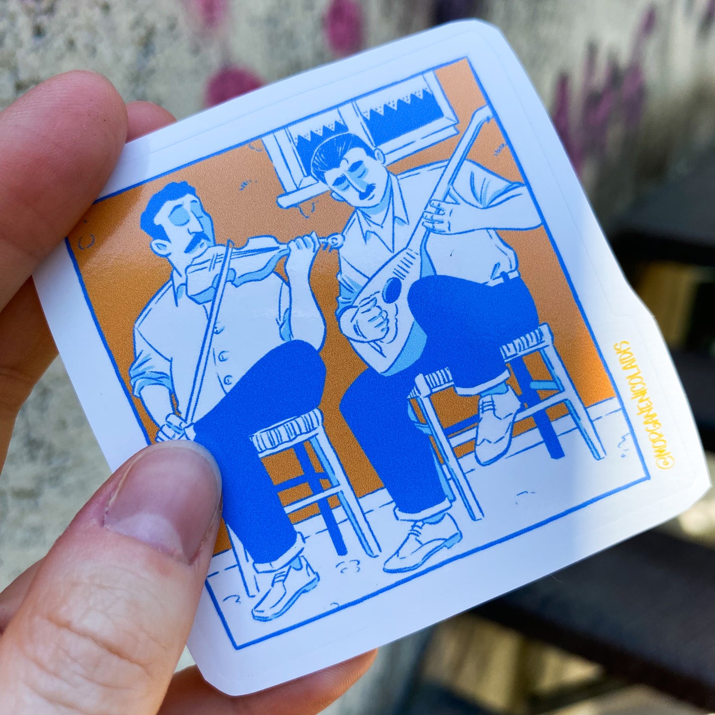 the sticker is hold by a hand. In background we can see a wall and part of stairs.