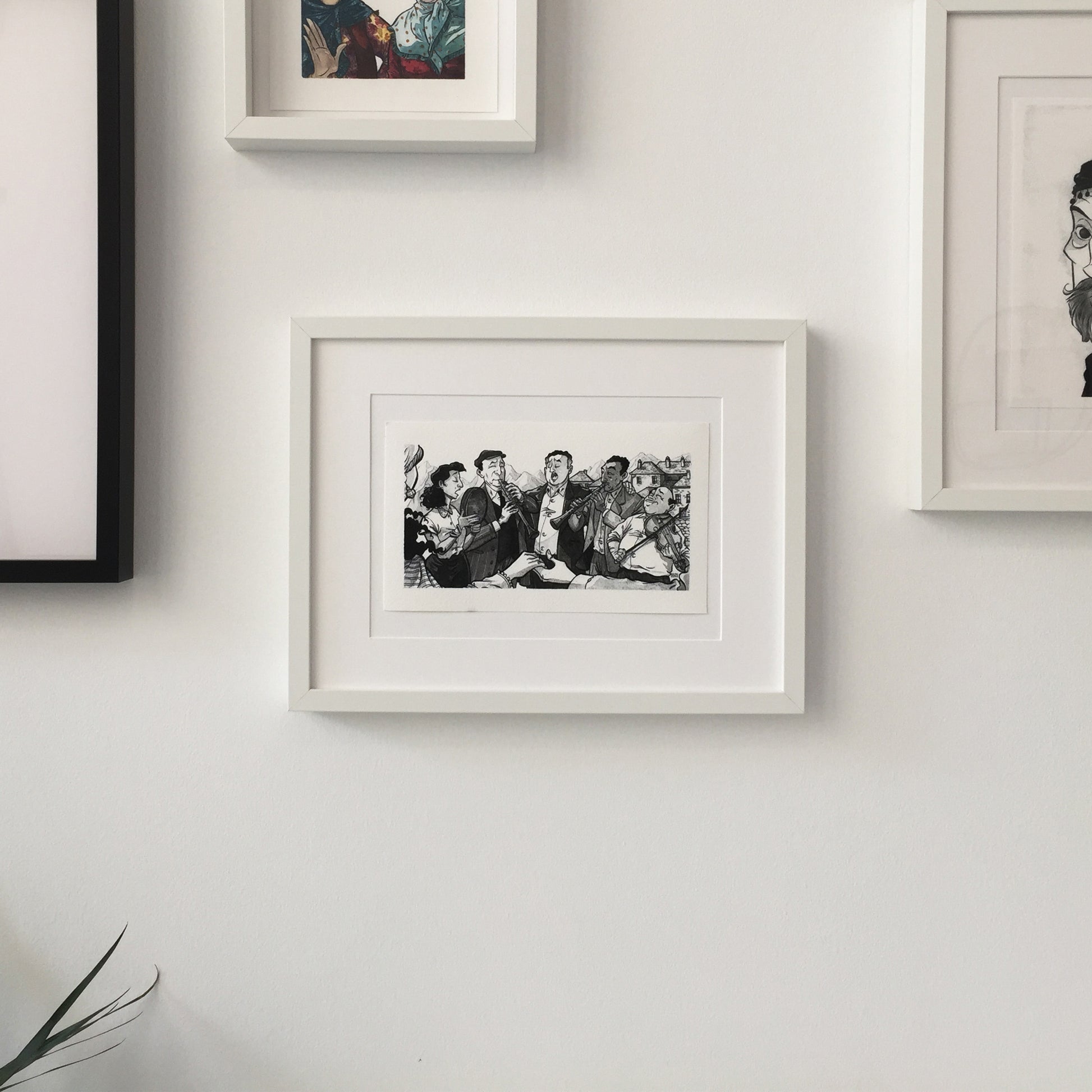 The illustration framed and hung on a wall with some other framed artworks.