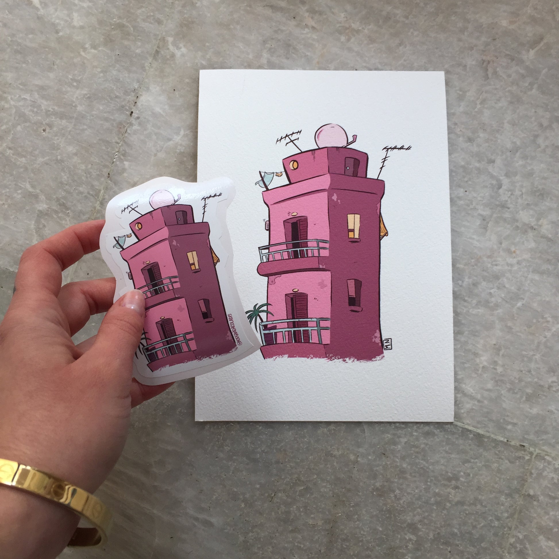 The sticker is hold by a hand above the art print of the sticker.