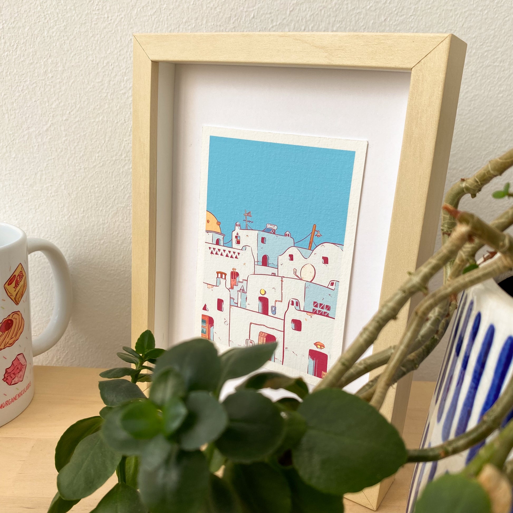 the print is placed on a small frame, on a wooden bench. On the first plan we have some plant on a decorative vase, at the left of the photography we can also see one of my mug.