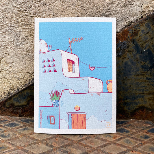 A small print placed in a metallic stair leaning against a wall. The print shows a few houses from a Cycladic Island.