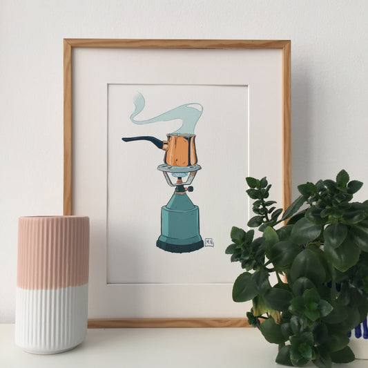 Framed art print of a briki and camping stove. Next to the frame we have a little decorative pot and a plant.